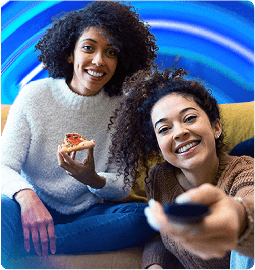 Duas pessoas olhando para uma tela, uma com uma pizza e a outra com o controle na mão